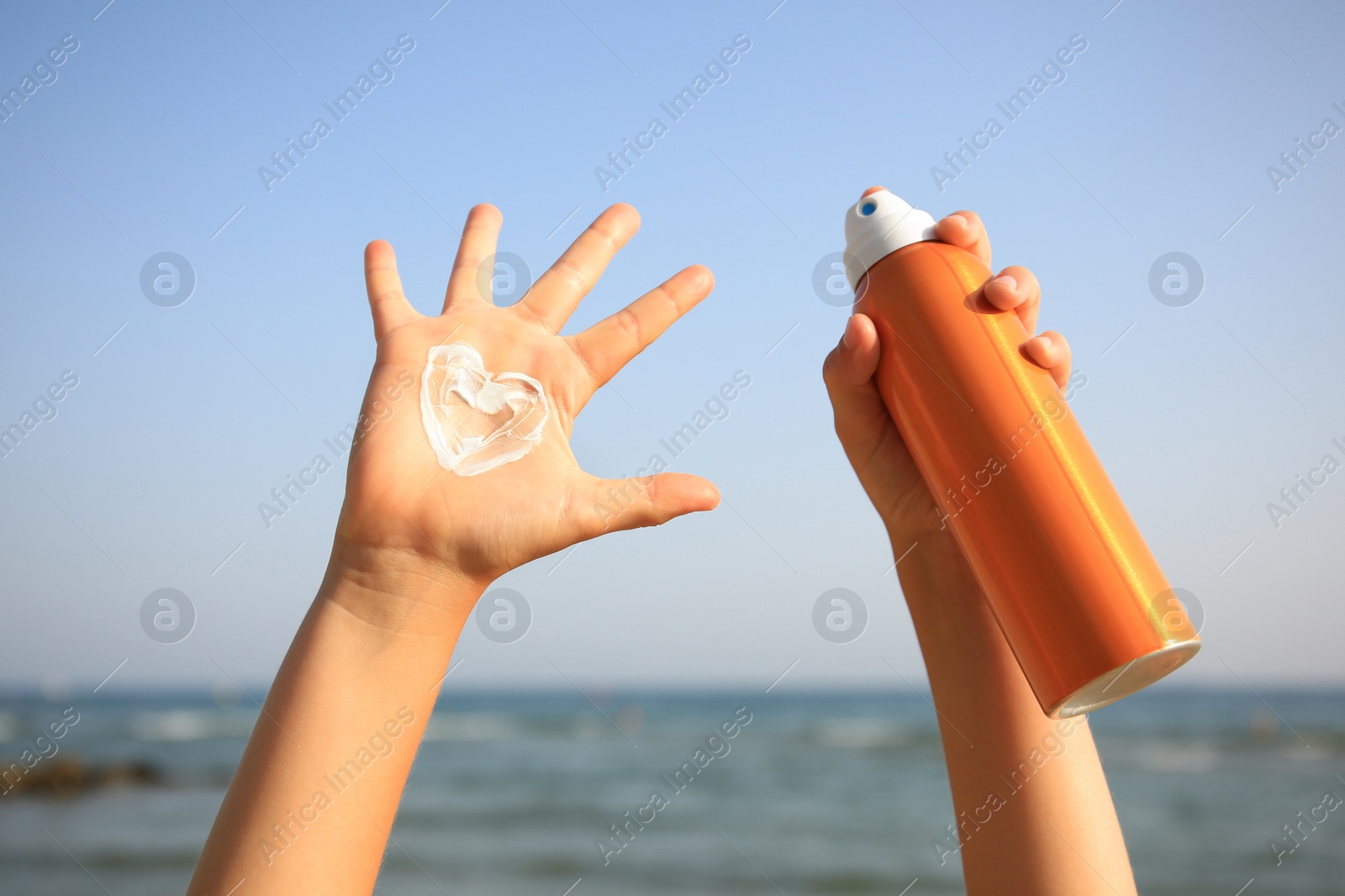 Photo of Child with bottle of sunscreen near sea, closeup. Sun protection care