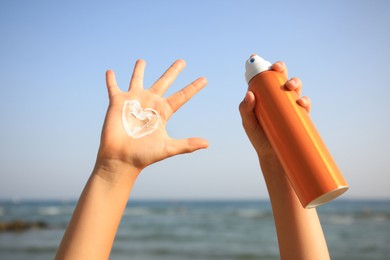 Child with bottle of sunscreen near sea, closeup. Sun protection care