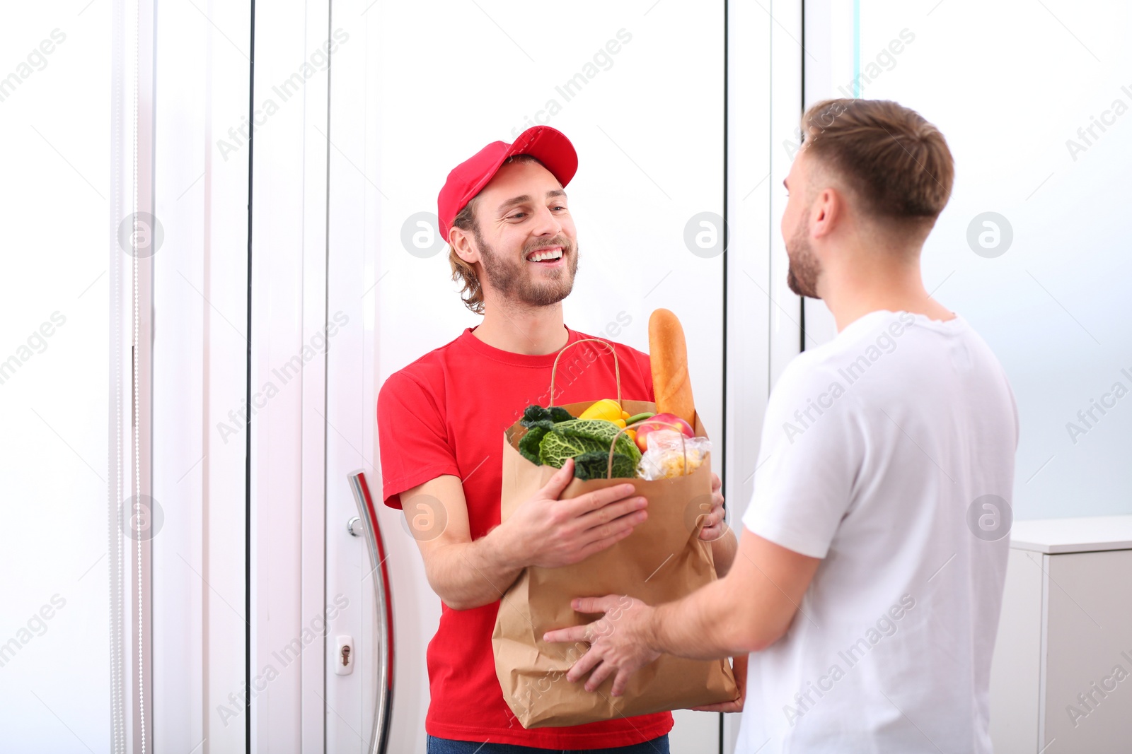 Photo of Courier giving paper bag with products to customer at home. Food delivery service