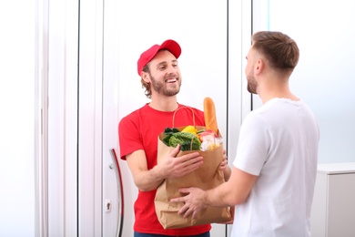 Photo of Courier giving paper bag with products to customer at home. Food delivery service