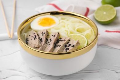 Bowl of delicious rice noodle soup with meat and egg on white textured table, closeup