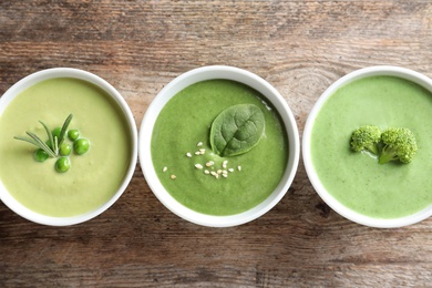 Dishes with different fresh vegetable detox soups made of green peas, broccoli and spinach on wooden background, flat lay