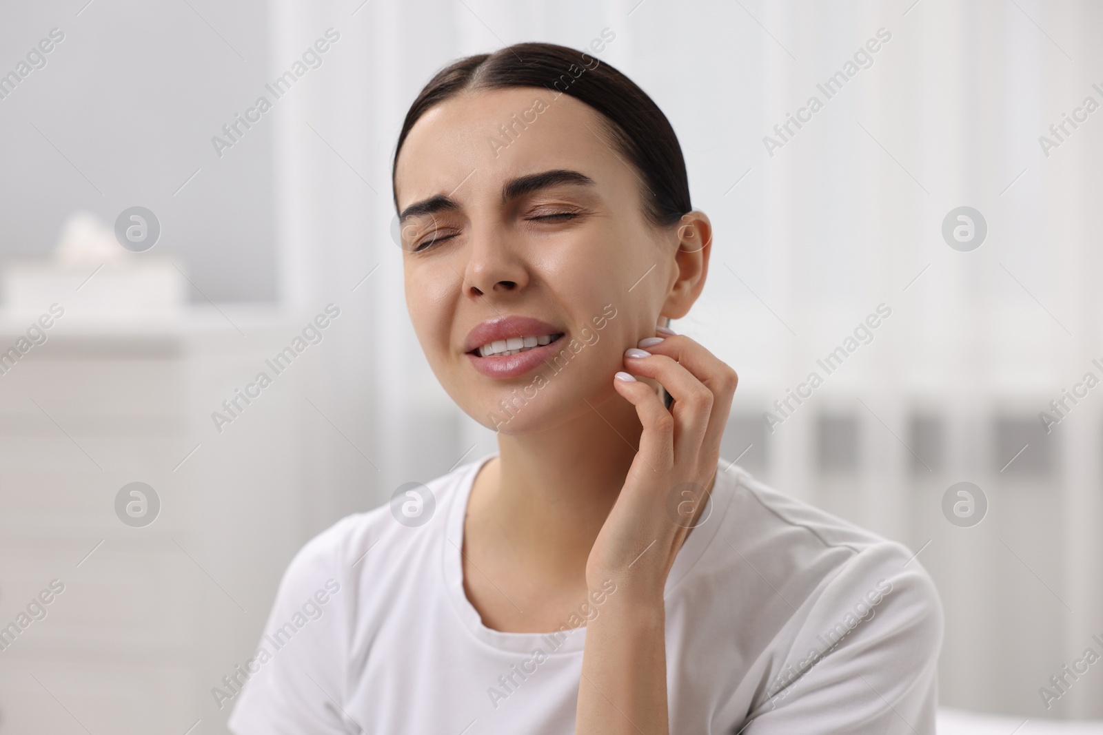Photo of Woman with dry skin scratching her face indoors