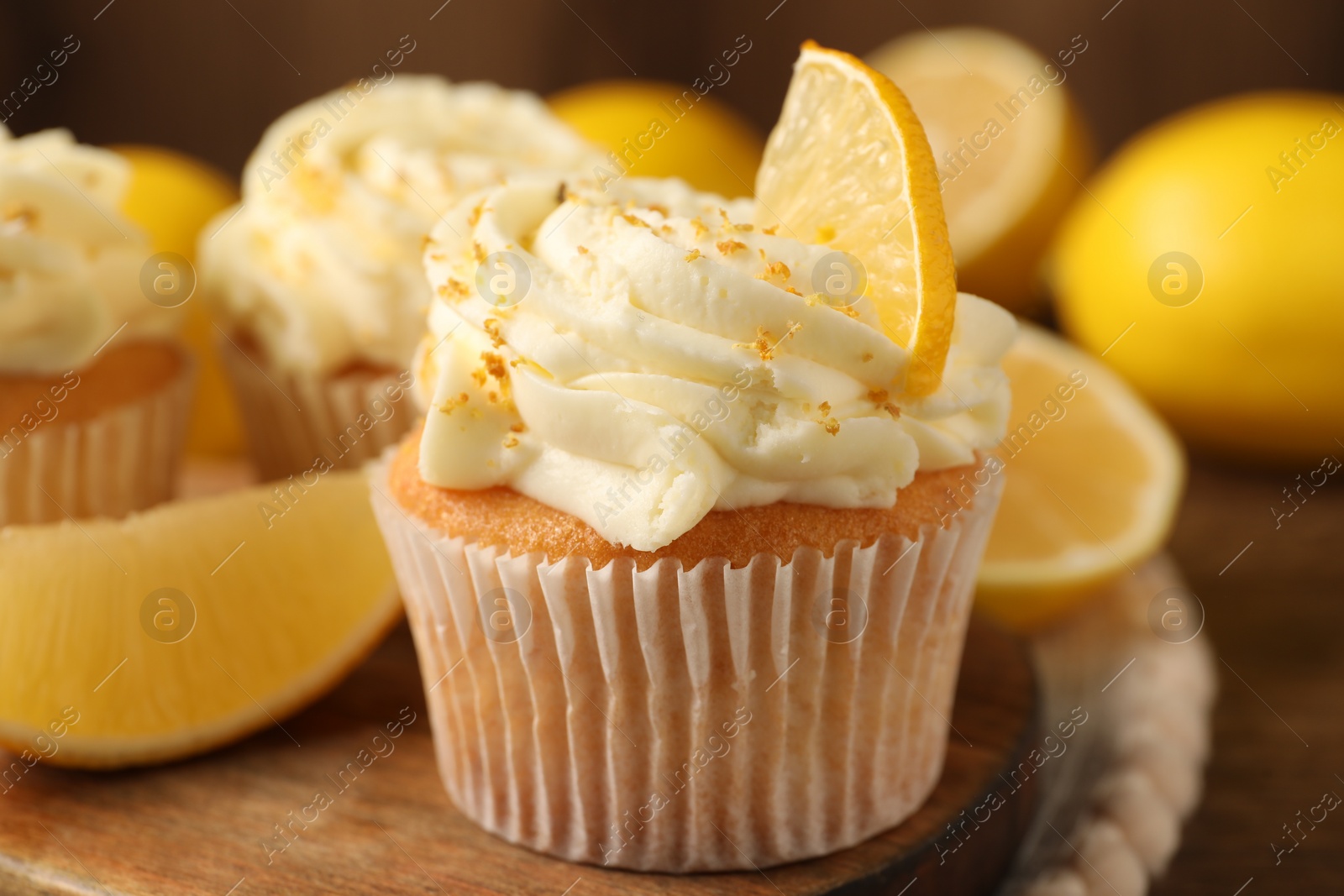 Photo of Tasty cupcakes with cream, zest and lemons on wooden table, closeup