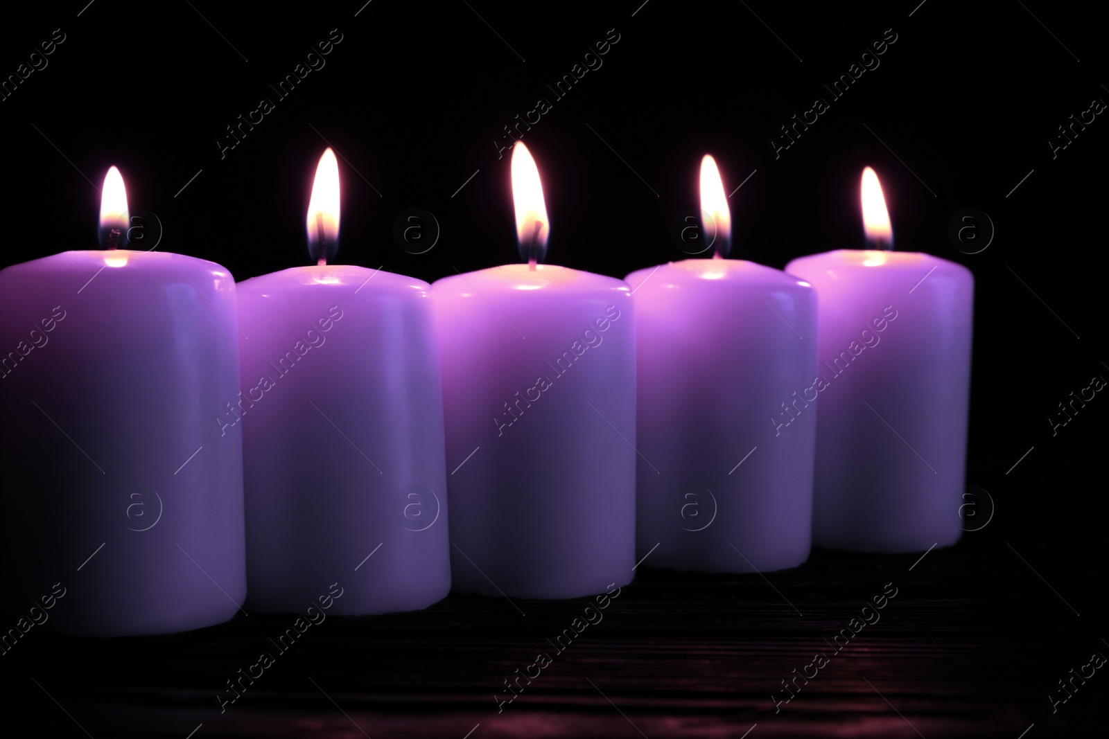 Image of Beautiful burning violet candles on black background. Funeral attributes