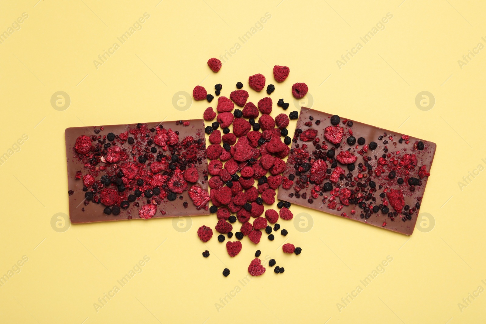 Photo of Chocolate with freeze dried fruits on yellow background, flat lay