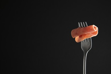 Photo of Fork with tasty slice of ham on black background, space for text