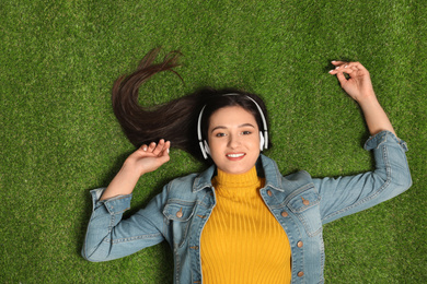Photo of Young woman listening to audiobook while lying on grass, top view