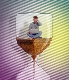 Worried man with laptop sitting inside hourglass on color background. Flowing sand symbolizing coming deadline