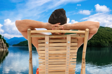 Image of Young man relaxing on sun lounger near river and mountains. Luxury vacation 