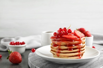 Delicious pancakes with fresh berries and syrup on grey table