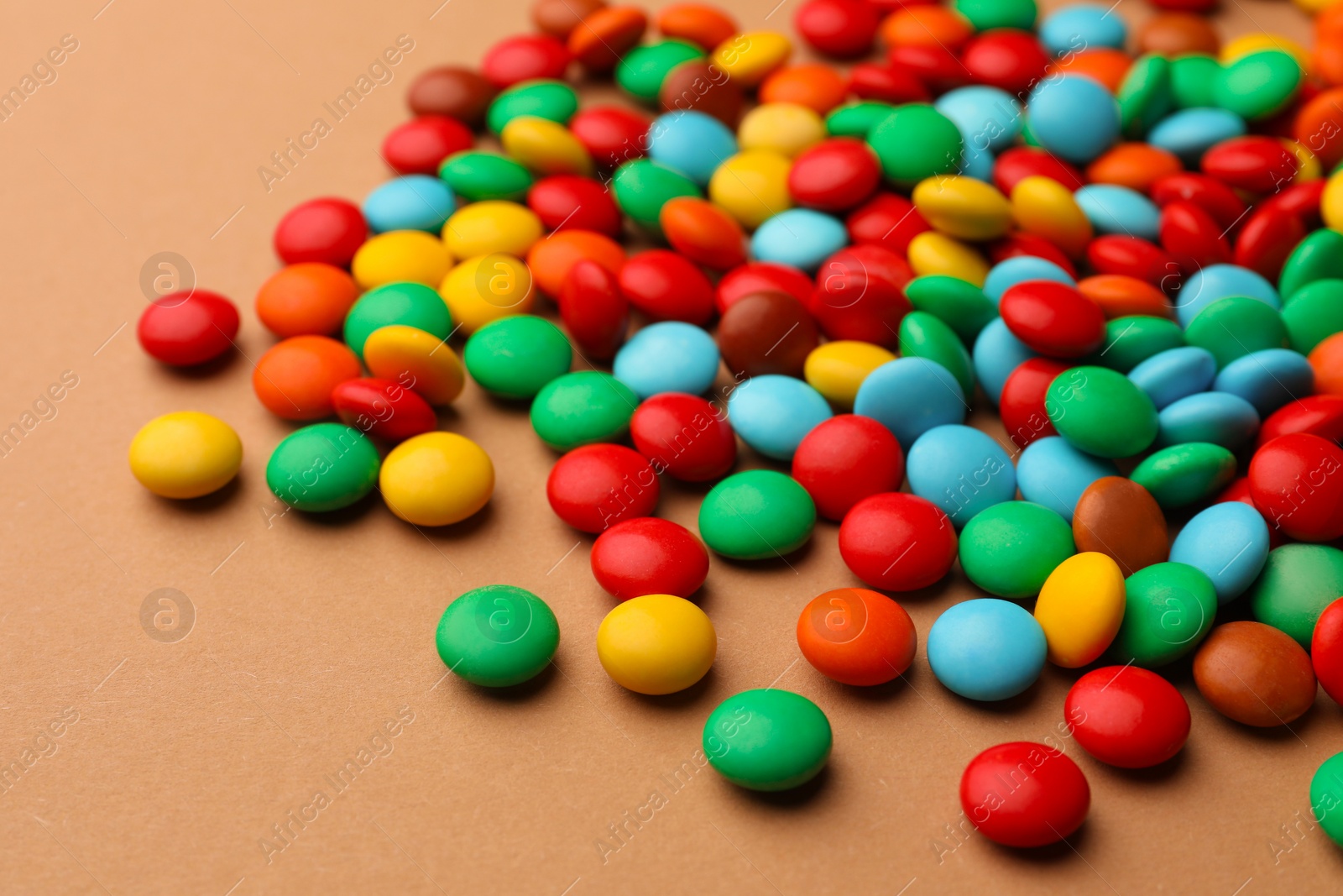 Photo of Tasty colorful candies on light brown background, closeup