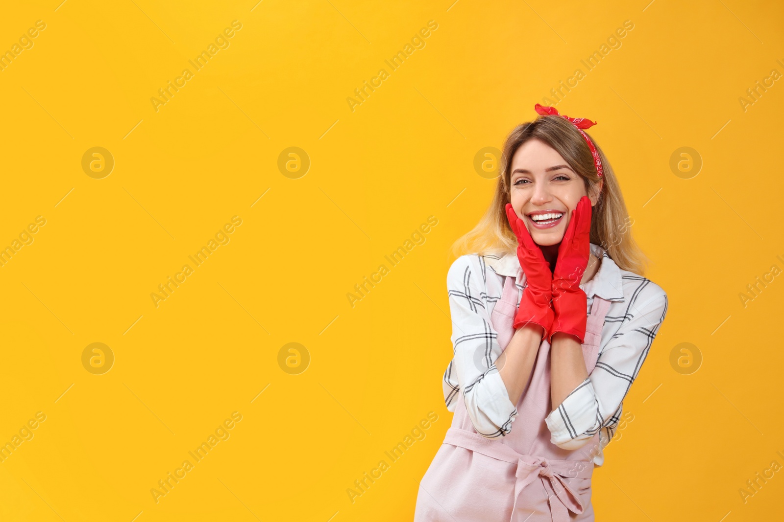 Photo of Young housewife in gloves on yellow background. Space for text