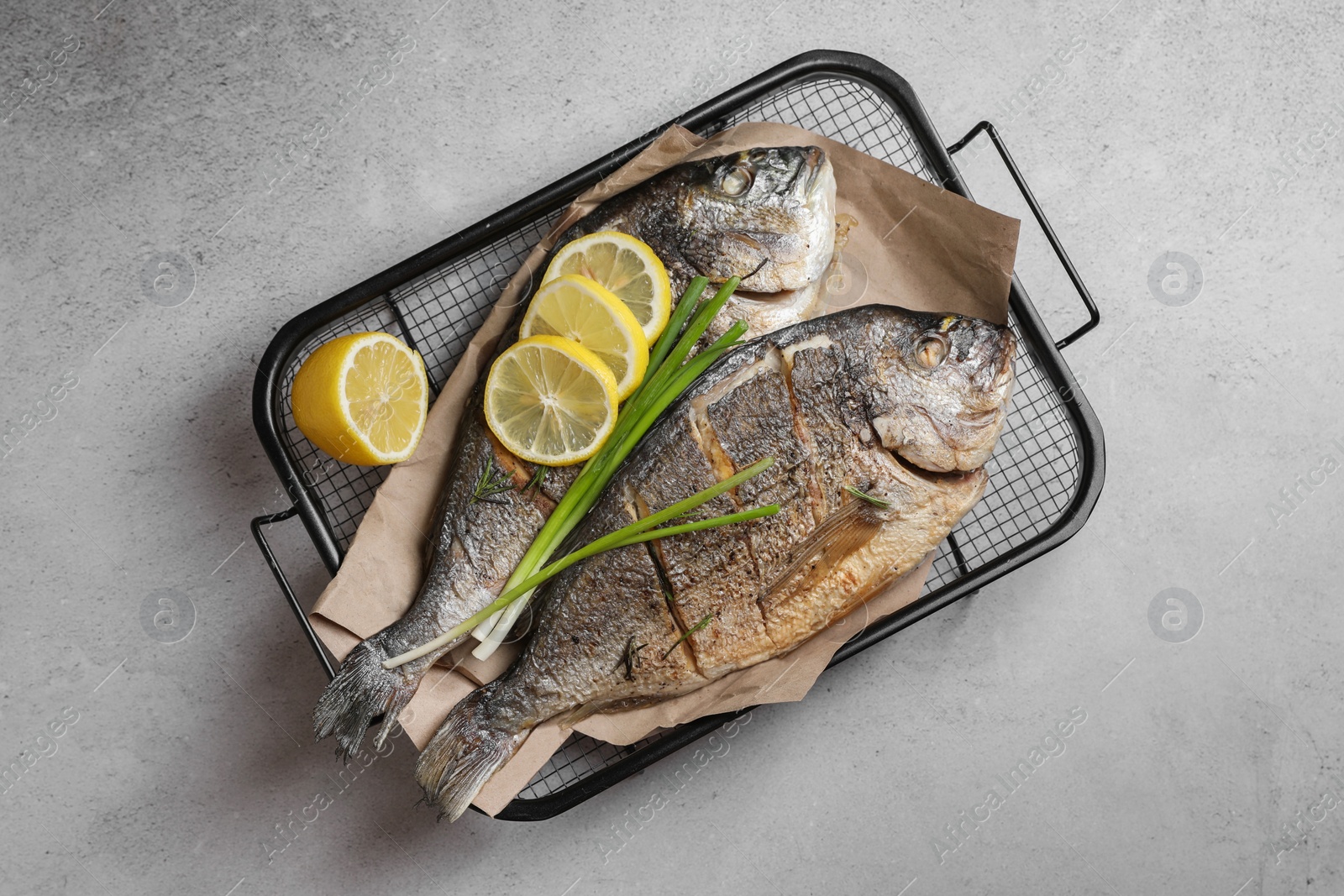 Photo of Seafood. Delicious baked fish served with green onion and lemon on light textured table, top view