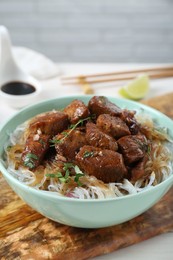 Photo of Bowl with pieces of soy sauce chicken and noodle on table, closeup