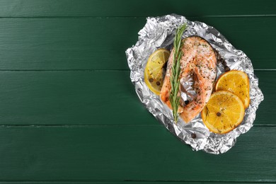 Tasty salmon baked in foil with citrus fruits and rosemary on green wooden table, top view. Space for text