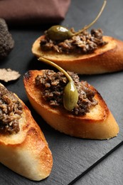 Photo of Tasty bruschettas with truffle paste and capers on black table, closeup