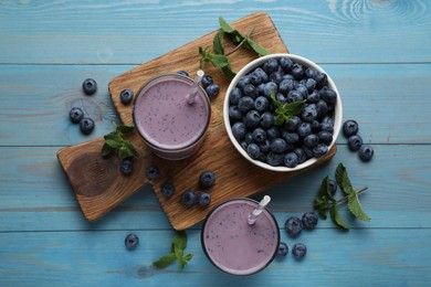 Glasses of blueberry smoothie with mint and fresh berries on turquoise wooden table, flat lay