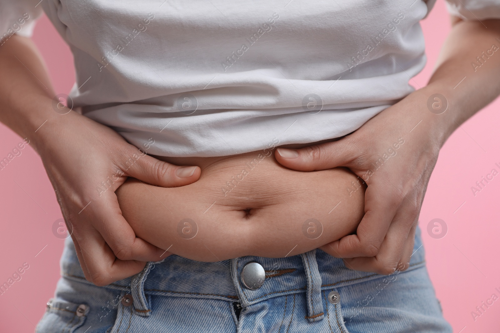 Photo of Woman touching belly fat on pink background, closeup. Overweight problem