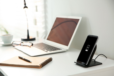 Photo of Mobile phone with wireless charger on white table. Modern workplace accessory
