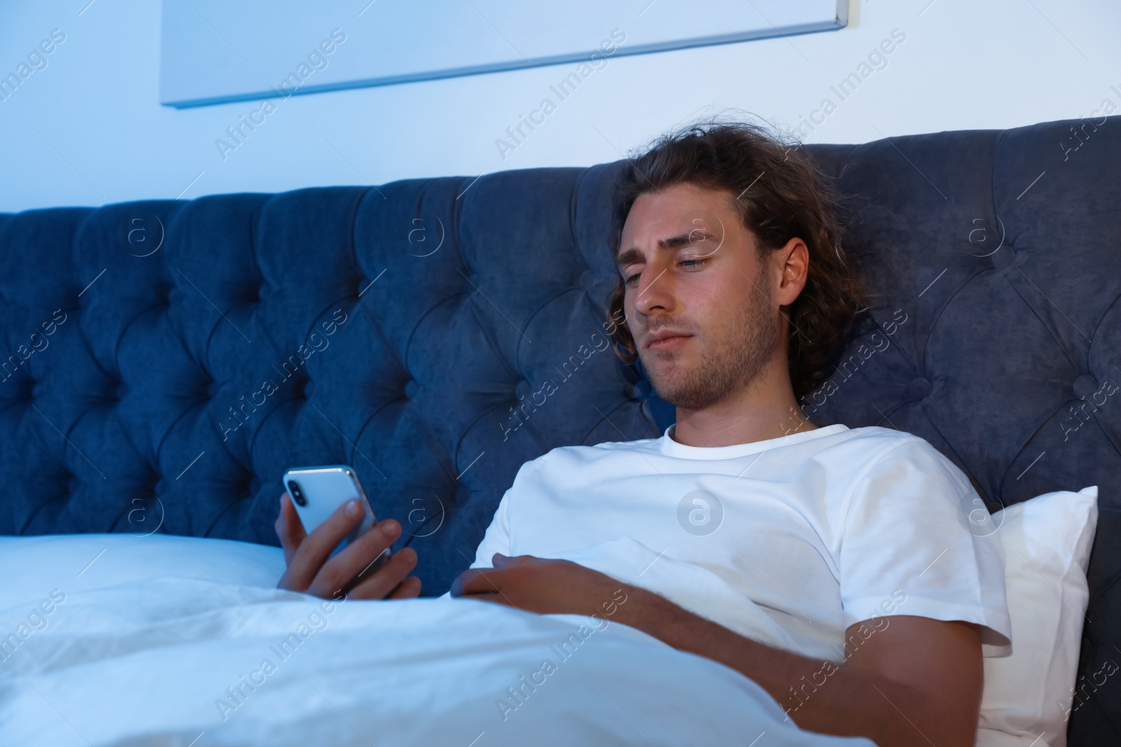 Photo of Handsome young man using smartphone in dark room at night. Bedtime