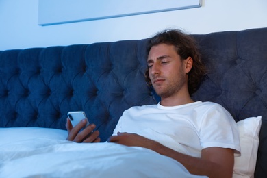 Handsome young man using smartphone in dark room at night. Bedtime