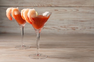 Photo of Tasty shrimp cocktail with sauce in glasses on wooden table, space for text