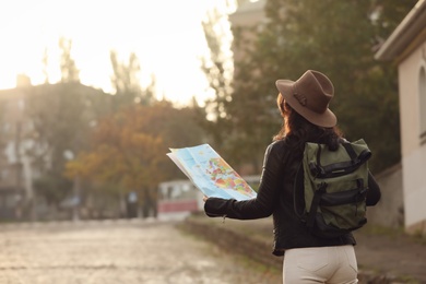 Traveler with map and backpack on city street, back view