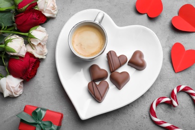 Photo of Cup of coffee, chocolate candies, roses and gift box on grey table, flat lay. Valentine's day breakfast