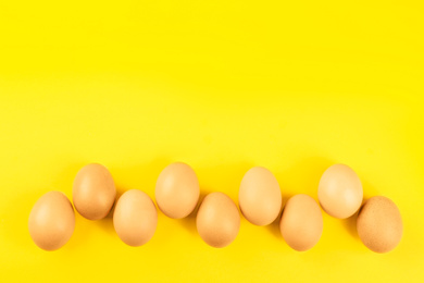 Raw chicken eggs on yellow background, flat lay. Space for text