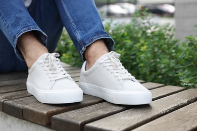 Photo of Man in stylish sneakers sitting on wooden bench outdoors, closeup