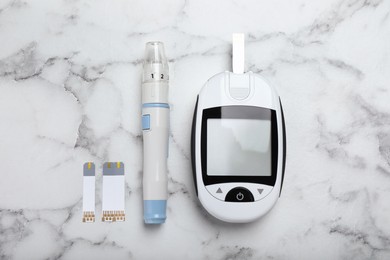 Glucometer, lancet pen and strips on white marble table, flat lay. Diabetes testing kit