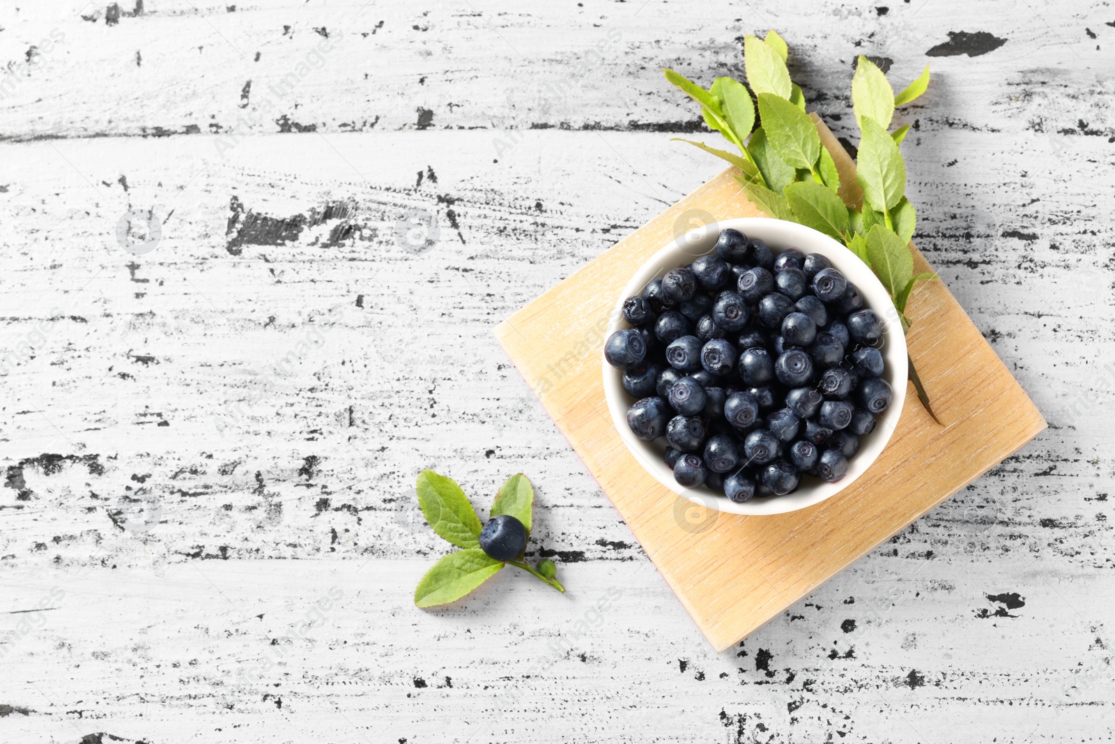 Photo of Bowl of tasty fresh bilberries and green leaves on old pink wooden table, flat lay. Space for text