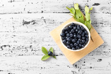 Bowl of tasty fresh bilberries and green leaves on old pink wooden table, flat lay. Space for text