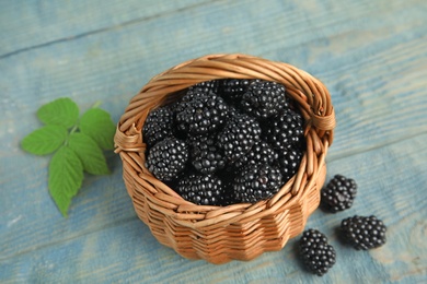 Photo of Wicker basket of tasty blackberries and leaves on blue wooden table