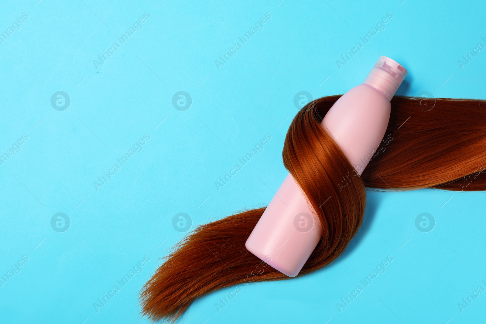 Photo of Shampoo bottle wrapped in lock of hair on light blue background, flat lay with space for text. Natural cosmetic products