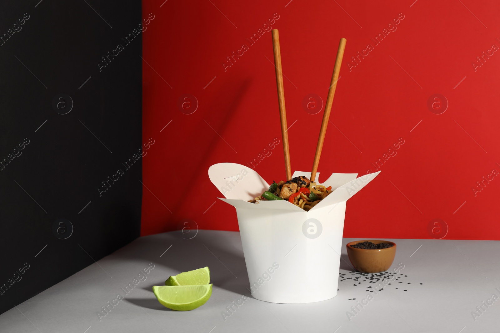 Photo of Box of wok noodles with vegetables, meat and chopsticks on color background