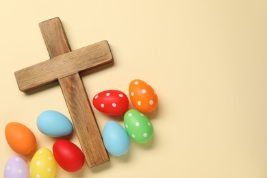 Wooden cross and painted Easter eggs on beige background, flat lay. Space for text