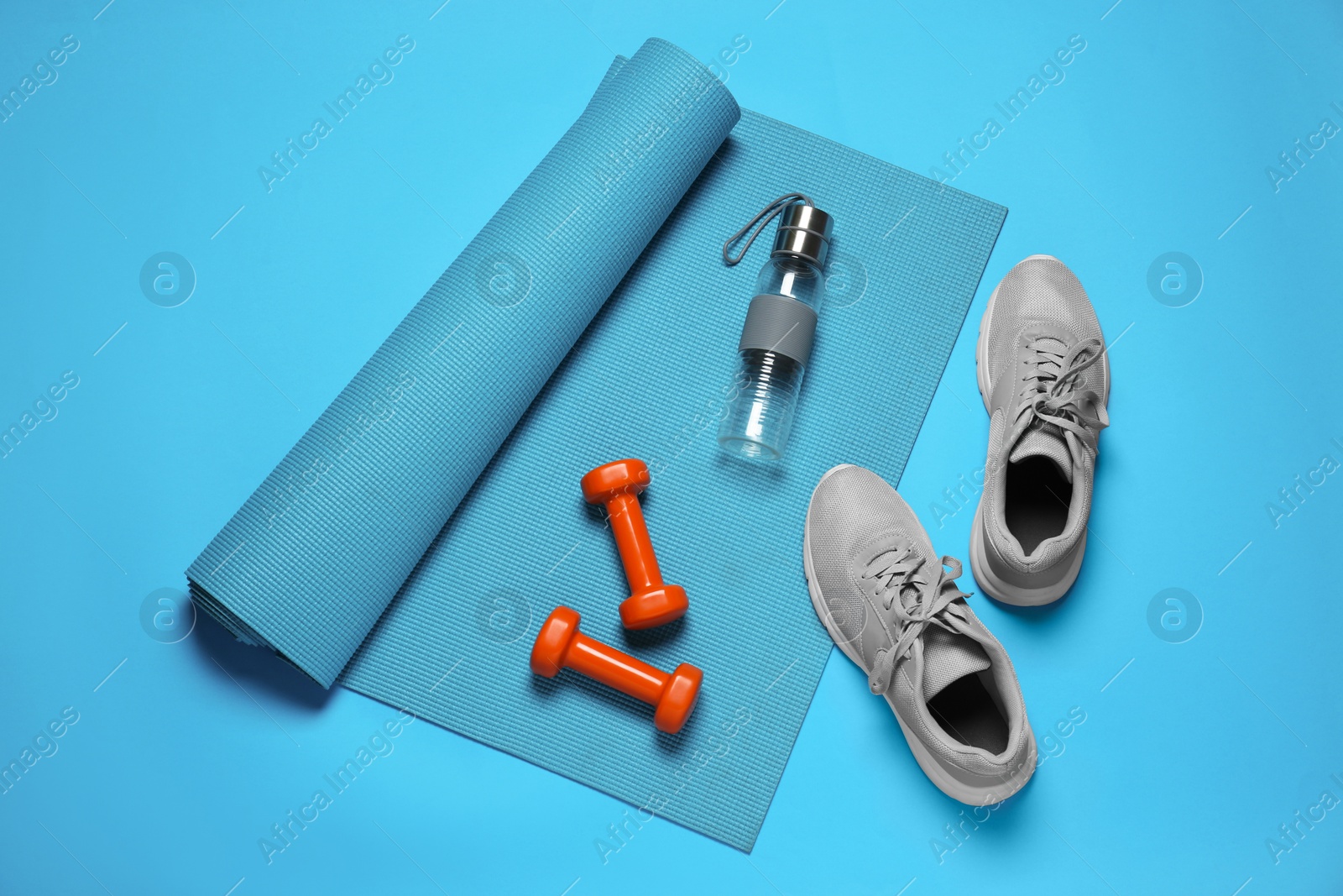 Photo of Exercise mat, dumbbells, shoes and bottle of water on turquoise background, flat lay