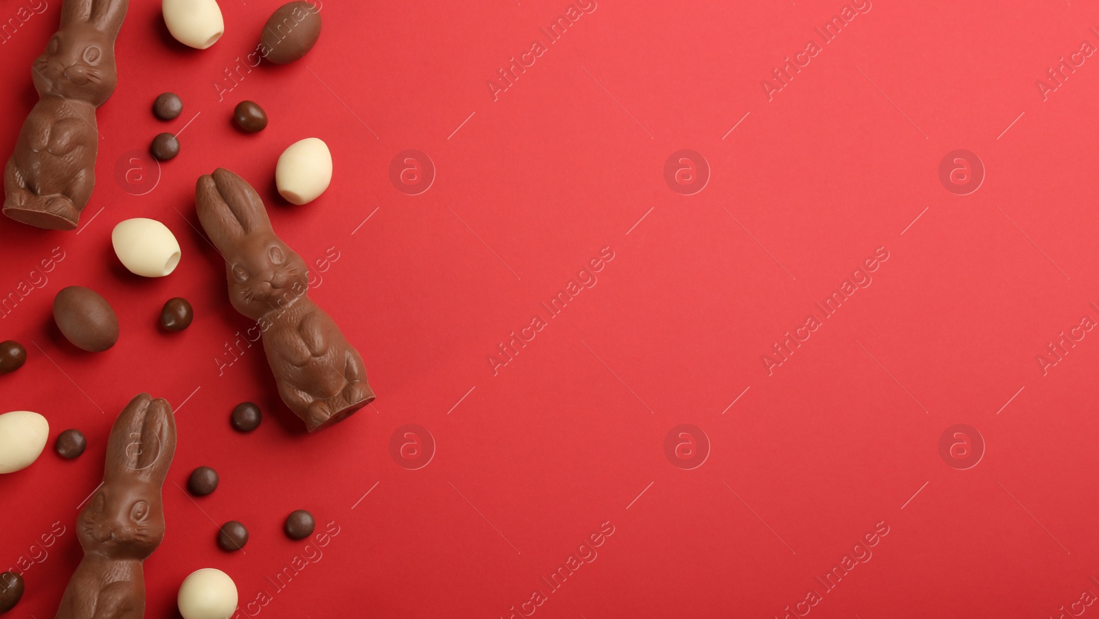 Photo of Flat lay composition with chocolate Easter bunnies, eggs and candies on red background. Space for text