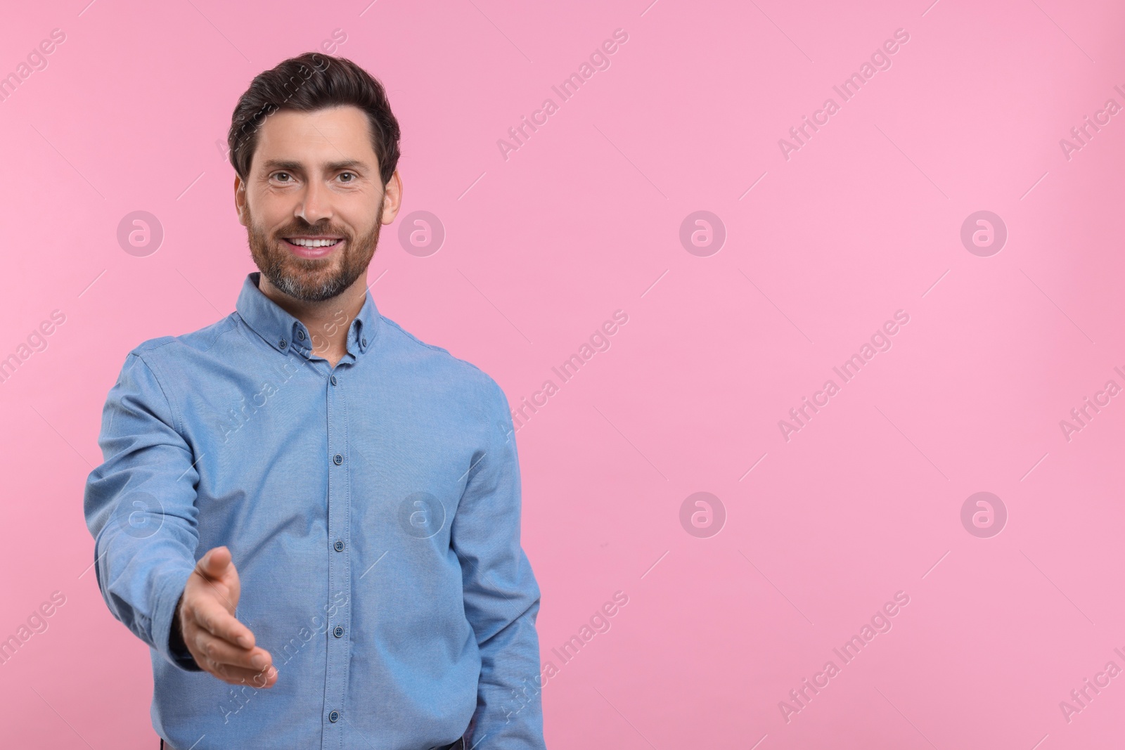 Photo of Happy man welcoming and offering handshake on pink background. Space for text