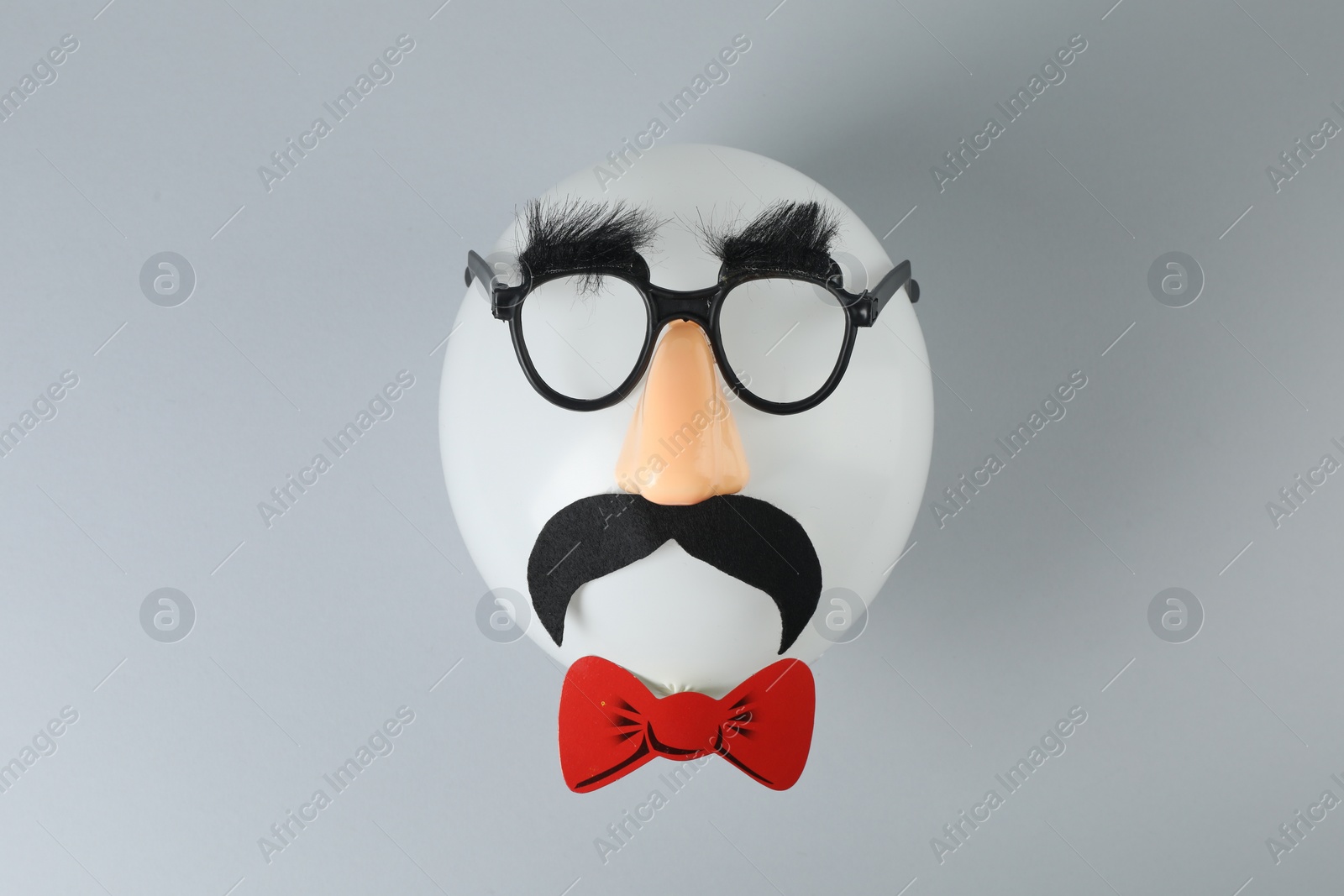 Photo of Man's face made of balloon, funny mask with fake mustache, nose and glasses on grey background, top view