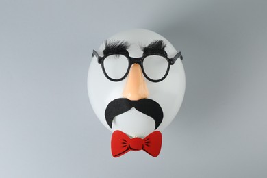 Man's face made of balloon, funny mask with fake mustache, nose and glasses on grey background, top view