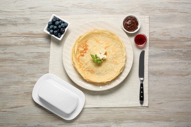 Photo of Delicious crepes with different products served on white wooden table, flat lay