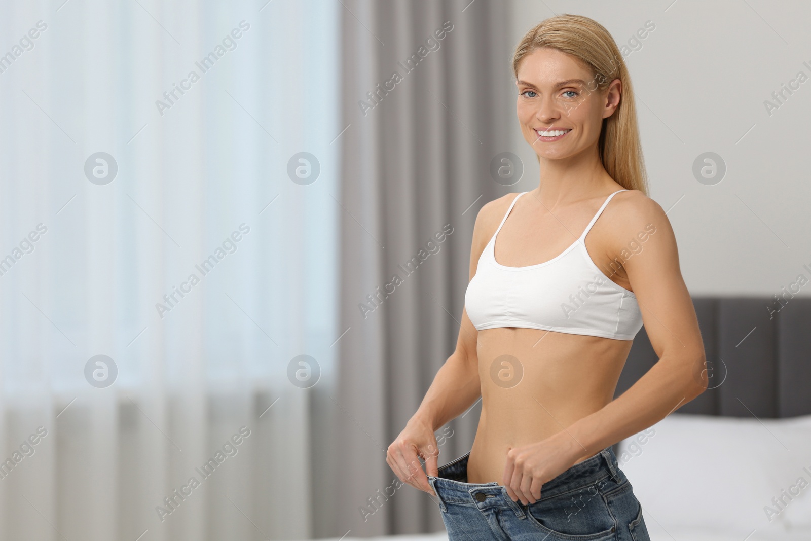 Photo of Slim woman wearing big jeans at home, space for text. Weight loss