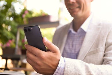 Businessman with smartphone in outdoor cafe, closeup