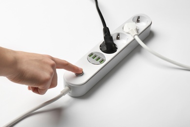 Woman pressing power button of extension cord on white background, closeup. Electrician's equipment