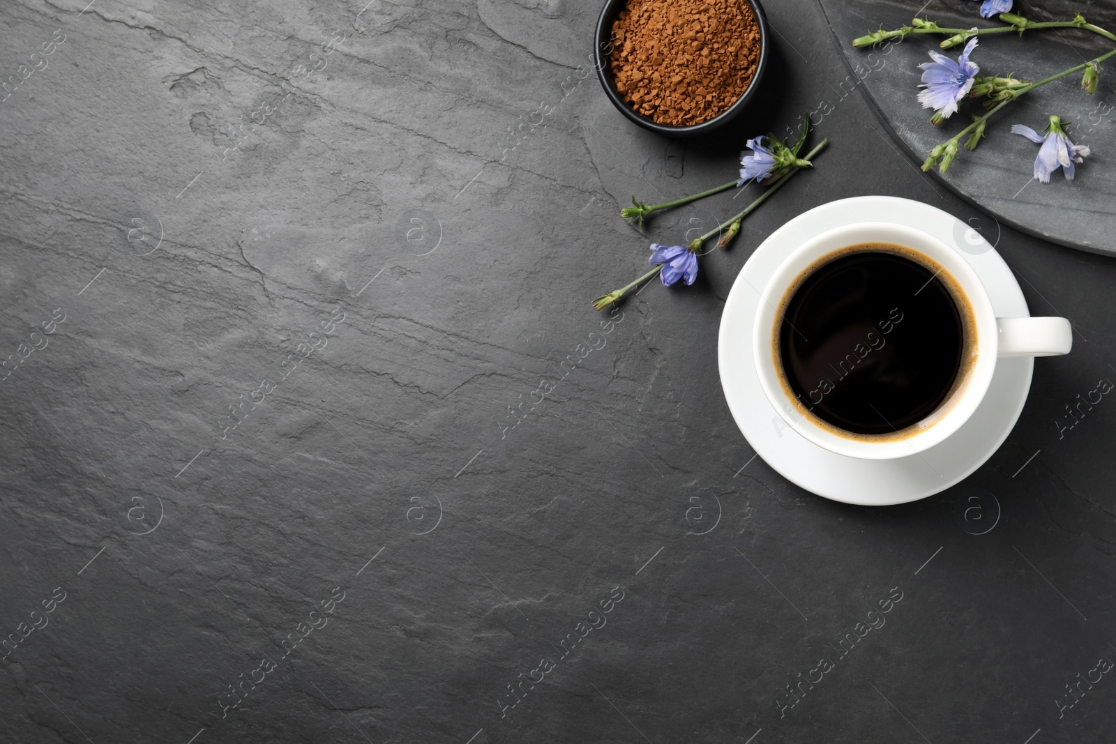 Photo of Cup of delicious chicory drink, granules and flowers on black table, flat lay. Space for text