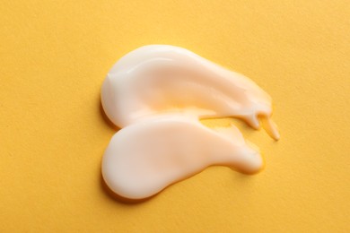 Photo of Samples of face cream on orange background, flat lay