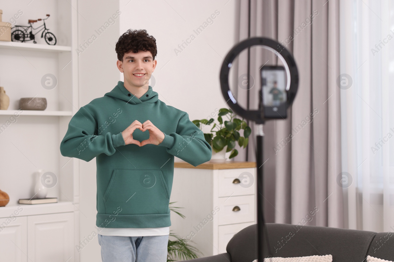 Photo of Smiling teenage blogger making heart gesture to his subscribers while streaming at home